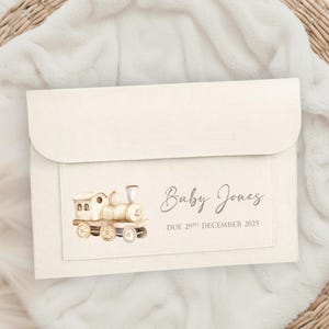 May include: A cream-coloured baby announcement card featuring a watercolour train illustration. The text reads "Baby Jones" and "Due 29th December 2025" in grey. The card is rectangular with a flap closure, suitable for a baby announcement.