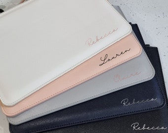 May include: Five personalized cosmetic bags in different colors. The bags are stacked on top of each other. The top bag is white with the name "Rebecca" written in pink. The second bag is pink with the name "Lauren" written in black. The third bag is gray with the name "Claire" written in pink. The fourth bag is dark blue with the name "Rebecca" written in white. The bottom bag is black with the name "Rebecca" written in white.