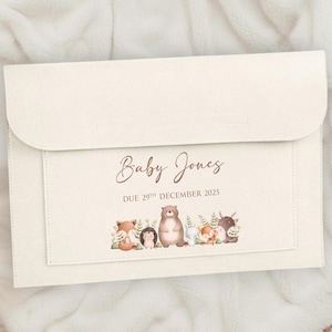 Może przedstawiać: Kremowa koperta z ogłoszeniem o narodzinach dziecka z klapką. Z przodu napis "Baby Jones" i "Due 29th December 2025". Akwarelowa ilustracja leśnych zwierząt zdobi dół.