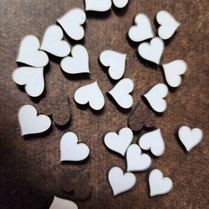Pu&ograve; includere: Una collezione di cuori di legno bianco sparsi su una superficie marrone. I cuori sono di diverse dimensioni e forme.