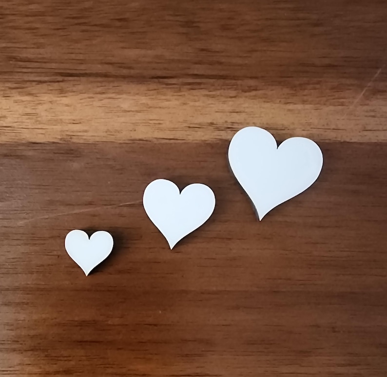 Pu&ograve; includere: Tre cuori di carta bianca di diverse dimensioni su una superficie di legno marrone.
