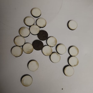 May include: A collection of small, round, white ceramic tiles with a slightly aged appearance. Some tiles have a brown, textured backing. The tiles are scattered on a white surface.
