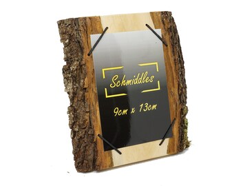 Könnte beinhalten: Rustikaler Holzbilderrahmen mit natürlichem Rindenrand. Der Rahmen enthält einen schwarzen Einsatz mit dem Text "Schmiddles" und den Maßen 9 cm x 13 cm. Schwarze Gummibänder sichern den Einsatz. Der Rahmen ist vor weißem Hintergrund.