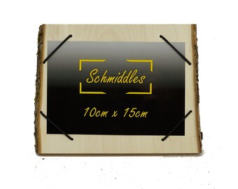 Könnte beinhalten: Ein Holzrahmen mit schwarzem Hintergrund und dem Text "Schmiddles" in einem gelben Kasten. Der Rahmen ist 10 cm x 15 cm groß und hat einen natürlichen Holzrindenrand.