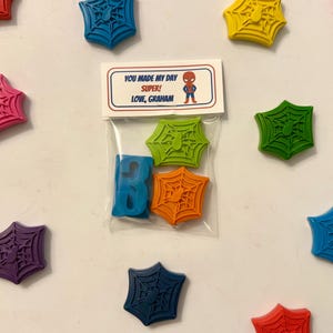 May include: A collection of colorful, spiderweb-shaped wax melts and a blue letter "B" in a clear bag. The bag has a label with the text "YOU MADE MY DAY SUPER! LOVE, GRAHAM" and a Spider-Man graphic.