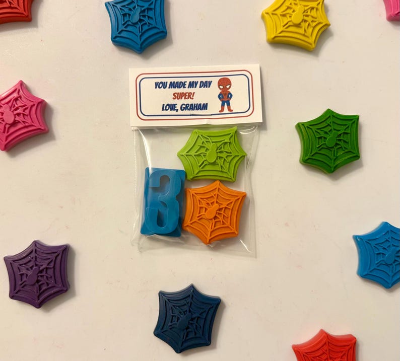 May include: A collection of colorful, spiderweb-shaped wax melts and a blue letter "B" in a clear bag. The bag has a label with the text "YOU MADE MY DAY SUPER! LOVE, GRAHAM" and a Spider-Man graphic.