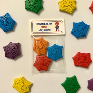 May include: A collection of colorful, spiderweb-shaped crayons in various colors, including blue, green, yellow, red, orange, purple, and pink. A small bag contains four crayons. A card reads "YOU MADE MY DAY SUPER! LOVE, HUDSON" with a Spider-Man graphic.
