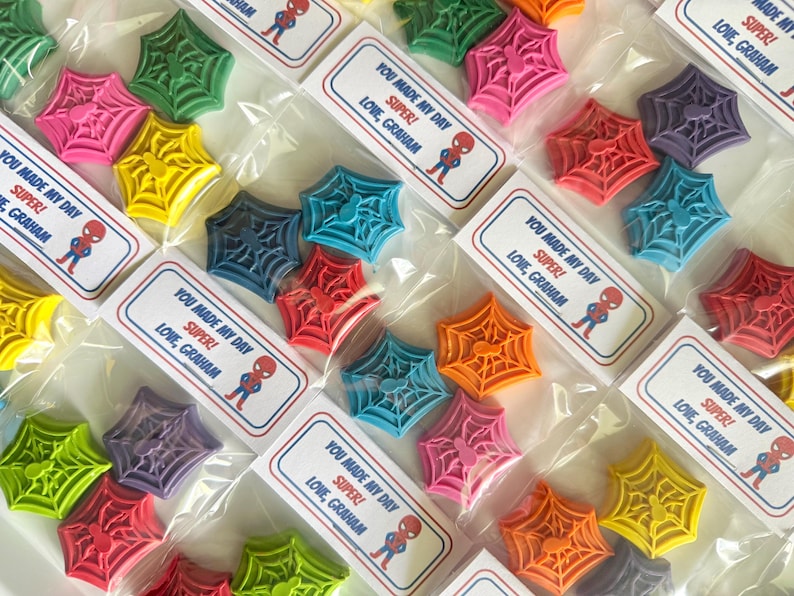 May include: Assortment of colorful, spiderweb-shaped items in clear plastic bags. Each bag has a label with the text "YOU MADE MY DAY SUPER! LOVE, GRAHAM" and a Spider-Man graphic. Colors include pink, green, yellow, blue, orange, and purple.