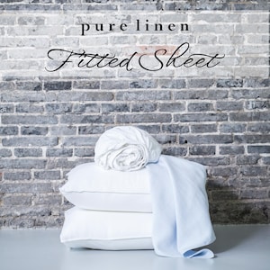 May include: A stack of white linen fitted sheets and a light blue linen throw blanket against a gray brick wall. The text "pure linen Fitted Sheet" is displayed above the linens.