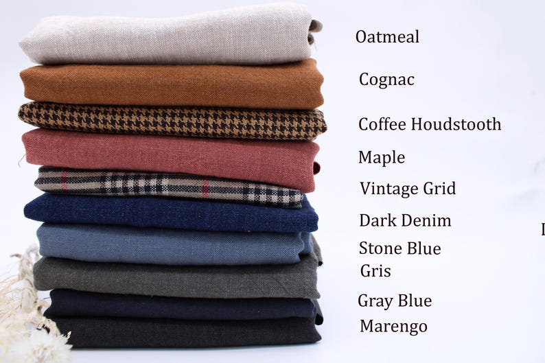 Pu&ograve; includere: Una pila di tessuti piegati in vari colori e motivi, etichettati come Oatmeal, Cognac, Coffee Houndstooth, Maple, Vintage Grid, Dark Denim, Stone Blue, Gris, Gray Blue e Marengo, disposti verticalmente su uno sfondo neutro.