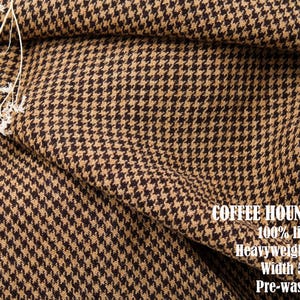 Pu&ograve; includere: Un tessuto con motivo pied-de-poule color marrone caff&egrave; e beige con una trama testurizzata. Il testo sul tessuto recita: COFFEE HOUNDSTOOTH, 100% linen, Heavyweight 9.2oz, Width 58", Pre-washed. Un piccolo rametto di fiori bianchi secchi poggia sul tessuto.