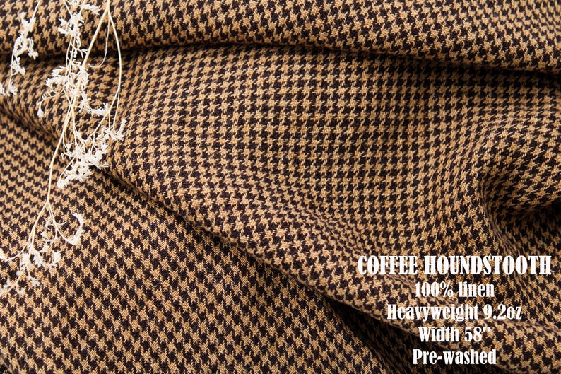 Pu&ograve; includere: Un tessuto con motivo pied-de-poule color marrone caff&egrave; e beige con una trama testurizzata. Il testo sul tessuto recita: COFFEE HOUNDSTOOTH, 100% linen, Heavyweight 9.2oz, Width 58", Pre-washed. Un piccolo rametto di fiori bianchi secchi poggia sul tessuto.