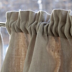May include: Close-up of a set of beige linen curtains with a rod hanging them. The curtains are gathered at the top and have a textured, woven look.