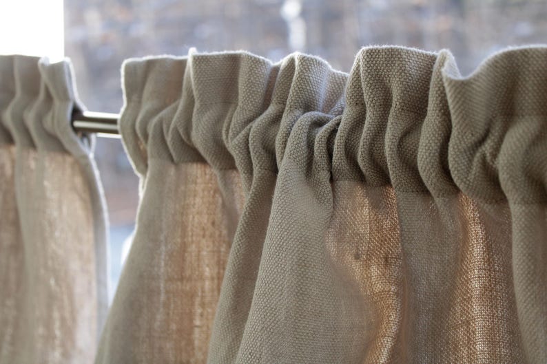 May include: Close-up of a set of beige linen curtains with a rod hanging them. The curtains are gathered at the top and have a textured, woven look.
