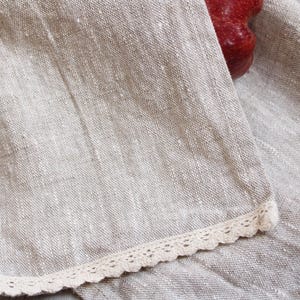 May include: A close-up of a beige linen fabric with a white lace trim. The fabric has a subtle texture and a slightly rough feel.