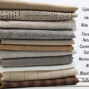 May include: A stack of folded fabric pieces in various neutral tones and patterns, including solid beige, dotted, striped, floral, and checkered designs. Text labels on the right list names: Caf&eacute; Cr&egrave;me, Ink trail, Wide stripes, Floral linen, Natural, Caramel sand, Oatmeal, Morning mist, White, Wheatfield check, and Coffee stripes.