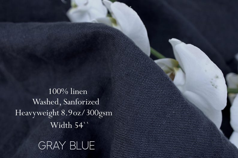 Pu&ograve; includere: Un pezzo di tessuto in lino 100% grigio blu con finitura lavata e sanforizzata. Il tessuto &egrave; pesante con 300 g/m&sup2; e ha una larghezza di 54 pollici. Fiori di orchidea bianchi sono posizionati lungo il bordo piegato del tessuto scuro.