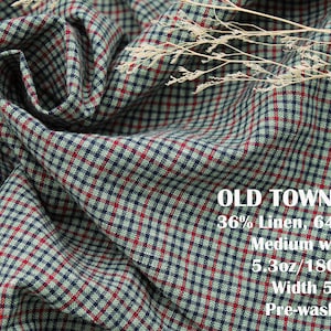 May include: A fabric with a plaid pattern in red, navy blue, and light green. Text on the fabric reads: OLD TOWN PLAID, 36% Linen, 64% cotton, Medium weight, 5.3oz/180gsm, Width 56", Pre-washed. A dried plant sprig rests on the folded textile surface.