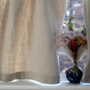 May include: A blue ceramic vase with a dried flower arrangement featuring white, pink, and red flowers. The vase is sitting on a windowsill with white curtains.