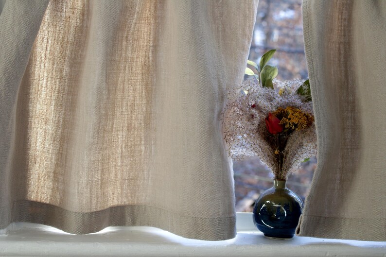 May include: A blue ceramic vase with a dried flower arrangement featuring white, pink, and red flowers. The vase is sitting on a windowsill with white curtains.