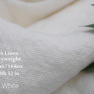 Pu&ograve; includere: Tessuto in lino 100% color bianco sporco, pesante e con una trama visibile. Il testo sul tessuto recita: 100% Linen, Heavyweight, 495gsm / 14.6oz, Width 52 in, Off White. Il materiale &egrave; piegato, mostrando una struttura di tessitura densa.
