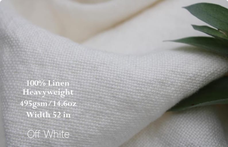 Pu&ograve; includere: Tessuto in lino 100% color bianco sporco, pesante e con una trama visibile. Il testo sul tessuto recita: 100% Linen, Heavyweight, 495gsm / 14.6oz, Width 52 in, Off White. Il materiale &egrave; piegato, mostrando una struttura di tessitura densa.