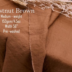 May include: Chestnut brown fabric with a visible weave texture. Text on the fabric reads: Chestnut Brown, Medium-weight, 153gsm/4.5oz, Width 56", Pre-washed. A sprig of dried white flowers rests on the top edge of the folded brown textile.