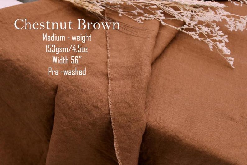 May include: Chestnut brown fabric with a visible weave texture. Text on the fabric reads: Chestnut Brown, Medium-weight, 153gsm/4.5oz, Width 56", Pre-washed. A sprig of dried white flowers rests on the top edge of the folded brown textile.