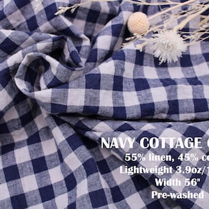 May include: Navy blue and white gingham check fabric with a soft, draped texture. Text on the fabric reads: NAVY COTTAGE CHECK, 55% linen, 45% cotton, Lightweight 3.9oz/132gs, Width 56", Pre-washed. A small cluster of dried white flowers rests on top.
