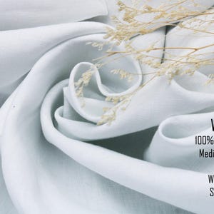 May include: White 100% linen fabric with a medium-weight of 6.6oz and a width of 58 inches. The softened fabric is draped in folds and accented with a sprig of dried flowers. The text on the image reads: White, 100% linen fabric, Medium-weight, 6.6oz, Width 58", Softened.
