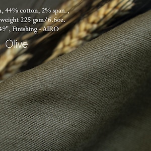 May include: Close-up of olive-colored fabric with a diagonal ribbed texture. The fabric is 49 inches wide and made of 54% linen, 44% cotton, and 2% span. The medium weight is 6.6oz. The text "Olive" is visible.