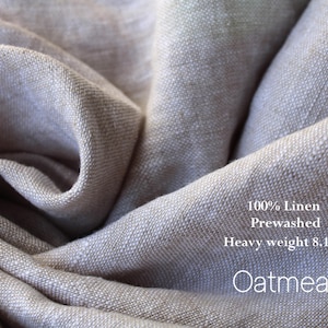 May include: Close-up of a folded, light gray linen fabric. The fabric is labeled "100% Linen Prewashed Heavy weight 8.1oz Oatmeal". The linen has a textured appearance and is tightly woven.