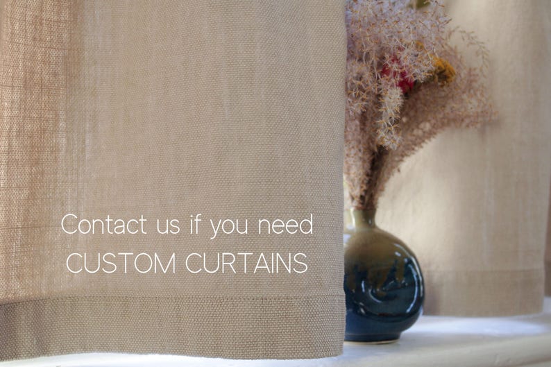 May include: A close-up of a pair of beige linen curtains with the text "Contact us if you need CUSTOM CURTAINS" printed on them. The curtains are hanging in a window with a vase of dried flowers in the background.