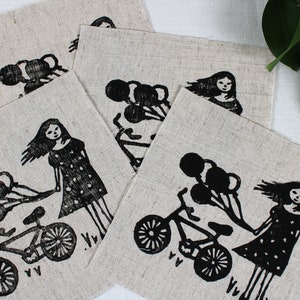 Peut inclure: Ensemble de quatre torchons en lin avec un imprimé noir et blanc d'une fille à vélo avec des ballons. La fille porte une robe à pois et a les cheveux longs. Le texte "V.V." est imprimé sur les torchons.