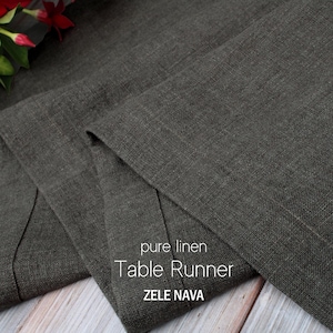 May include: A dark gray pure linen table runner with the text "pure linen Table Runner ZELE NAVA". The runner is folded, showing its texture and a hint of red flowers.