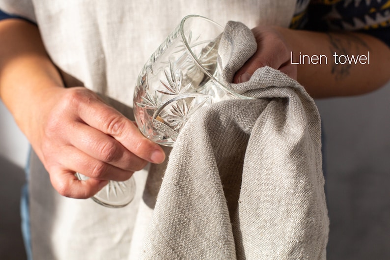 May include: A person is drying a clear glass with a linen towel. The towel is beige and has a rough texture. The glass has a decorative pattern.