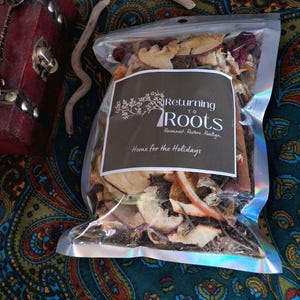 May include: A cellophane bag filled with dried fruit and spices. The bag has a brown label with the text "Returning to Roots" and "Home for the Holidays". The bag is on a colourful paisley patterned fabric.