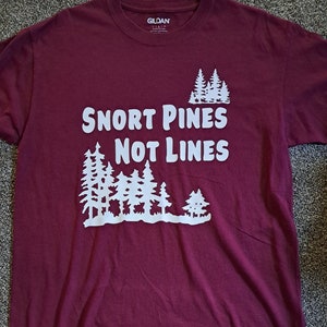May include: A maroon t-shirt with a white graphic design that says "Snort Pines Not Lines" and features a row of pine trees.
