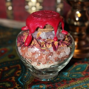 Może przedstawiać: Szklany słoik wypełniony różową solą himalajską, suszonymi płatkami róż i czerwoną pieczęcią woskową. Słoik stoi na kolorowym wzorzystym materiale.