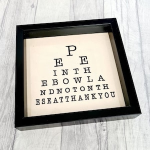 May include: Black framed wall art with a white background and black text that reads "P E E I N T H E B O W L A N D N O T O N T H E S E A T T H A N K Y O U".