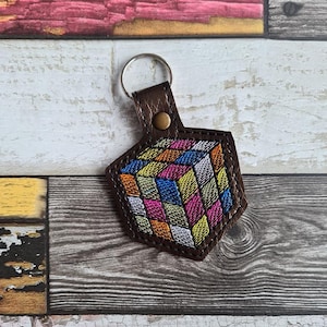 May include: A brown leather keychain with a colorful embroidered Rubik's Cube design.