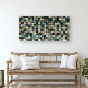 Puede incluir: Una pieza de arte de pared de madera con un mosaico de cuadrados en tonos de azul, verde y marrón. El arte está colgado sobre un banco de madera con dos almohadas blancas. Una almohada tiene el texto "welcome home".