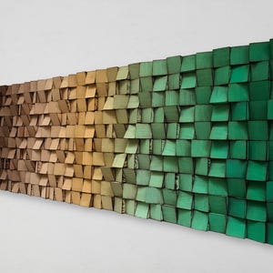 Puede incluir: Una pieza de arte de pared hecha de madera con un degradado de colores de marrón a verde. La madera está dispuesta en un patrón escalonado, creando una superficie texturizada.