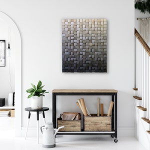 May include: A large, square, wooden wall art piece with a gradient color scheme, transitioning from light beige at the top to dark gray at the bottom. The artwork is composed of numerous small, square wooden blocks. The piece hangs above a wooden console table.