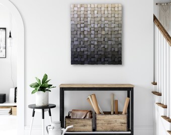 May include: A large, square, wooden wall art piece with a gradient colour scheme, transitioning from light beige at the top to dark grey at the bottom. The artwork is composed of numerous small, square wooden blocks. The piece hangs above a wooden console table.