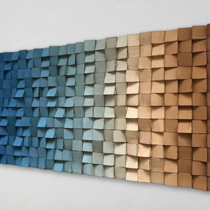 Puede incluir: Una pieza de arte de pared hecha de madera con un degradado de colores azul, gris y marrón. La madera está dispuesta en un patrón escalonado, creando una superficie texturizada.