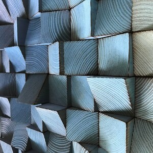 以下が含まれることがあります： 青色の木製のブロックでできた壁の彫刻。ブロックは幾何学的なパターンで配置され、質感のある抽象的なデザインを生み出しています。
