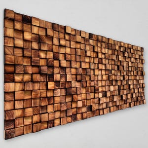 Puede incluir: Una gran pieza de arte mural rectangular compuesta por numerosos bloques de madera cuadrados y pequeños. Los bloques están dispuestos en un patrón de mosaico, mostrando la veta natural de la madera y diferentes tonos de marrón y beige. La obra de arte tiene un efecto tridimensional.