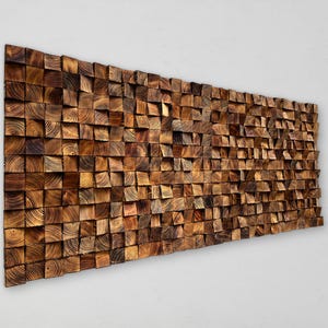 Könnte beinhalten: Ein großes, rechteckiges Wandkunstwerk aus Holz, das aus zahlreichen kleinen, quadratischen Blöcken besteht. Die Blöcke sind in verschiedenen Brauntönen gehalten und erzeugen einen strukturierten, dreidimensionalen Effekt. Die Holzmaserung ist sichtbar.
