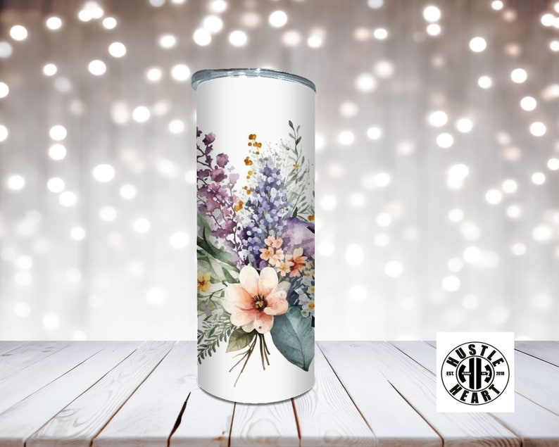 May include: White stainless steel tumbler with a floral design featuring purple, pink, and green watercolor flowers. The tumbler has a black lid and a black logo that says "Hustle Heart" with a barbell symbol.